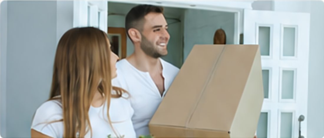 Stel met een verhuisdoos bij de voordeur van hun nieuwe woning